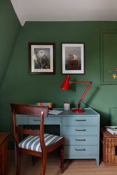 a room with green walls and two pictures on the wall next to a blue desk