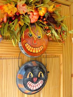 two pumpkins with faces painted on them are hanging from a wooden wall next to other decorations