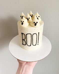 a hand holding a cake decorated with white frosting and black sprinkles