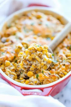 a spoon full of corn casserole with cheese and herbs on top in a red dish