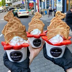 three people holding up cups filled with ice cream and waffles in the shape of fish