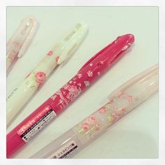 three pens sitting next to each other on top of a white table with pink flowers