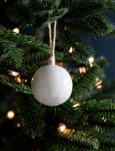 a white ornament hanging from the top of a christmas tree with lights on it