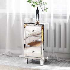 a mirrored side table with a vase on top and a small tree in the corner