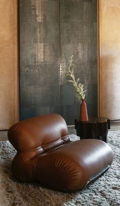 a brown leather chair and ottoman in front of a wall with a vase on it