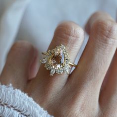 a woman's hand wearing a gold ring with an oval shaped diamond surrounded by smaller diamonds