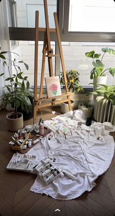 an easel, paintbrushes and other art supplies sit on the floor in front of a window