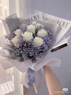 a bouquet of white roses and lavenders is held by someone's hand in front of a window