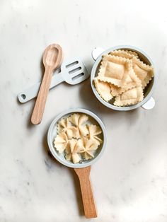 two bowls filled with food next to a wooden utensil on top of a white counter