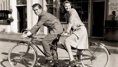 an old black and white photo of two people on a bicycle