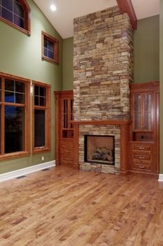 an empty living room with wood floors and stone fireplace in the center, surrounded by green walls