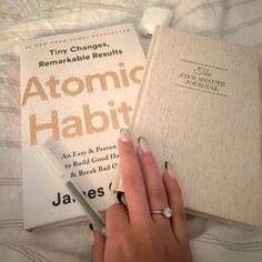 a woman's hand holding a pen next to an open book on top of a bed