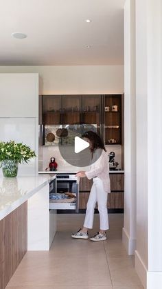 a woman standing in a kitchen next to an oven and counter top with flowers on it