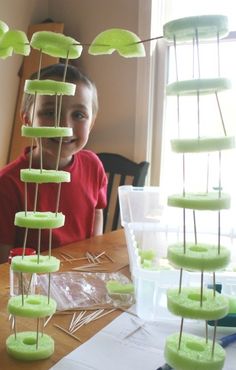 a young boy sitting in front of a table with green buttons and plastic cups on it