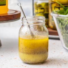 a glass jar filled with yellow liquid next to a salad