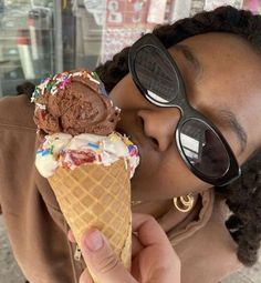 a woman wearing sunglasses is eating an ice cream cone with sprinkles and chocolate