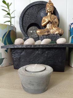 a buddha statue sitting on top of a wooden table next to rocks and a candle