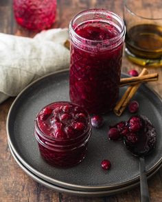 two jars of cranberry sauce sit on a plate with spoons next to them