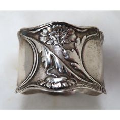 a silver ring with a flower and leaves on the front, sitting on a white surface