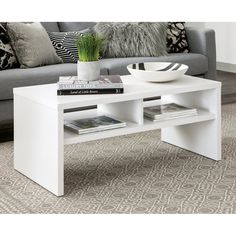 a white coffee table with books on it in front of a gray couch and pillows