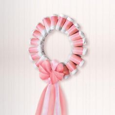 a pink and white ribbon is hanging on the wall next to a wreath with ribbons