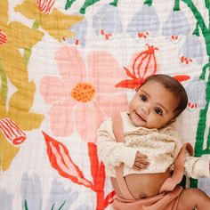 a baby is laying down on a colorful flowered blanket and smiling at the camera