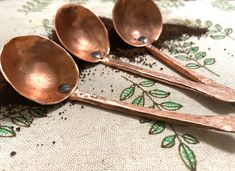 three antique spoons sitting on top of a cloth covered tablecloth with green leaves