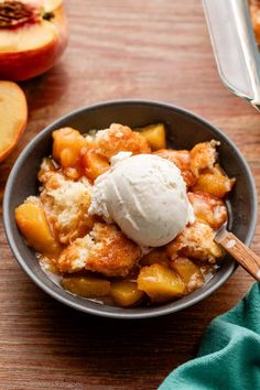 a bowl filled with fruit and ice cream on top of a wooden table next to sliced peaches