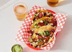 three tacos with meat and vegetables in a basket next to a glass of beer