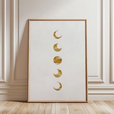 a white and gold framed art print with five phases of the moon on it in front of a wall