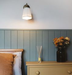 a vase with flowers sitting on top of a bed next to a night stand and lamp