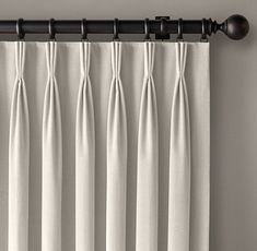 white curtains hanging on the side of a window in front of a curtain rod with black handles