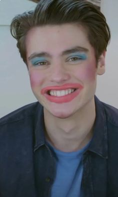 a young man with blue and pink makeup smiling at the camera while wearing a denim shirt