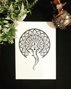 a white paper with a black design on it next to some flowers and a vase