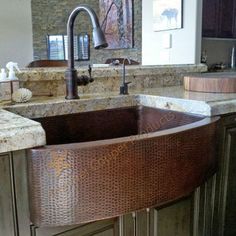 a kitchen sink with an apron style design in stainless steel and granite countertops, along with wooden cabinets