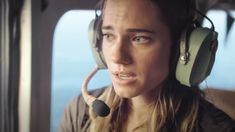 a woman wearing headphones sitting in an airplane looking out the window at the ocean