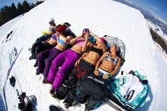 several women laying on the snow with their skis and backpacks in front of them