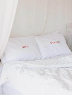 a bed with white sheets and red embroidered pillows