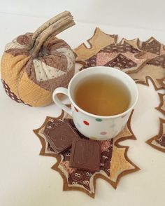 a cup of tea sits next to some decorative coasters and a pumpkin shaped cookie