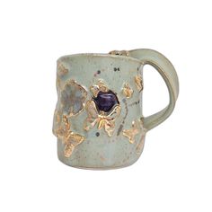 a ceramic mug with gold and purple designs on it's sides, sitting against a white background