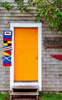 an orange door sits in front of a gray building with two canoes on it