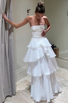 a woman in a white dress standing next to a curtain and looking at her cell phone