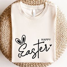 a white t - shirt with the words happy and easter printed on it next to a woven basket