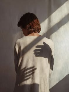 a woman standing in front of a white wall with her shadow on the wall behind her