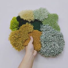 a hand is holding several different colored rugs on a white surface, each with various colors and sizes