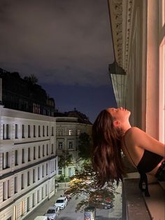 a woman leaning up against a window sill looking out at the street below her