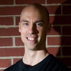 a bald man standing in front of a brick wall