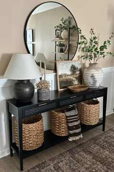 a black console table with baskets under a large round mirror on the wall above it