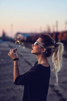 a woman holding a sparkler in her right hand and looking up at the sky