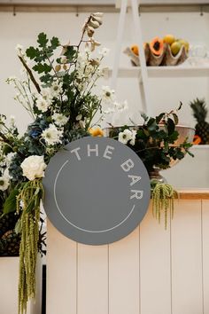 a sign that says the bar with flowers and greenery on display in front of it